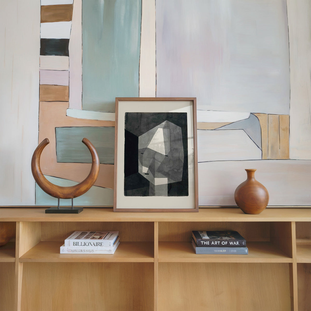 Gray faceted crystal head watercolor abstract print in a walnut frame on an oak shelf beside a wooden crescent sculpture