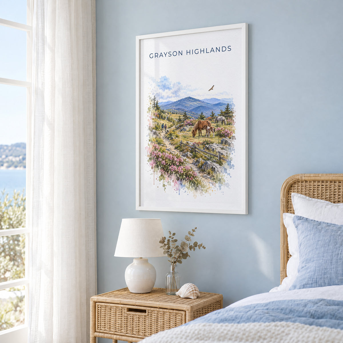 Grayson Highlands State Park watercolor print in a white frame on a pale blue wall beside a rattan bed in a coastal bedroom