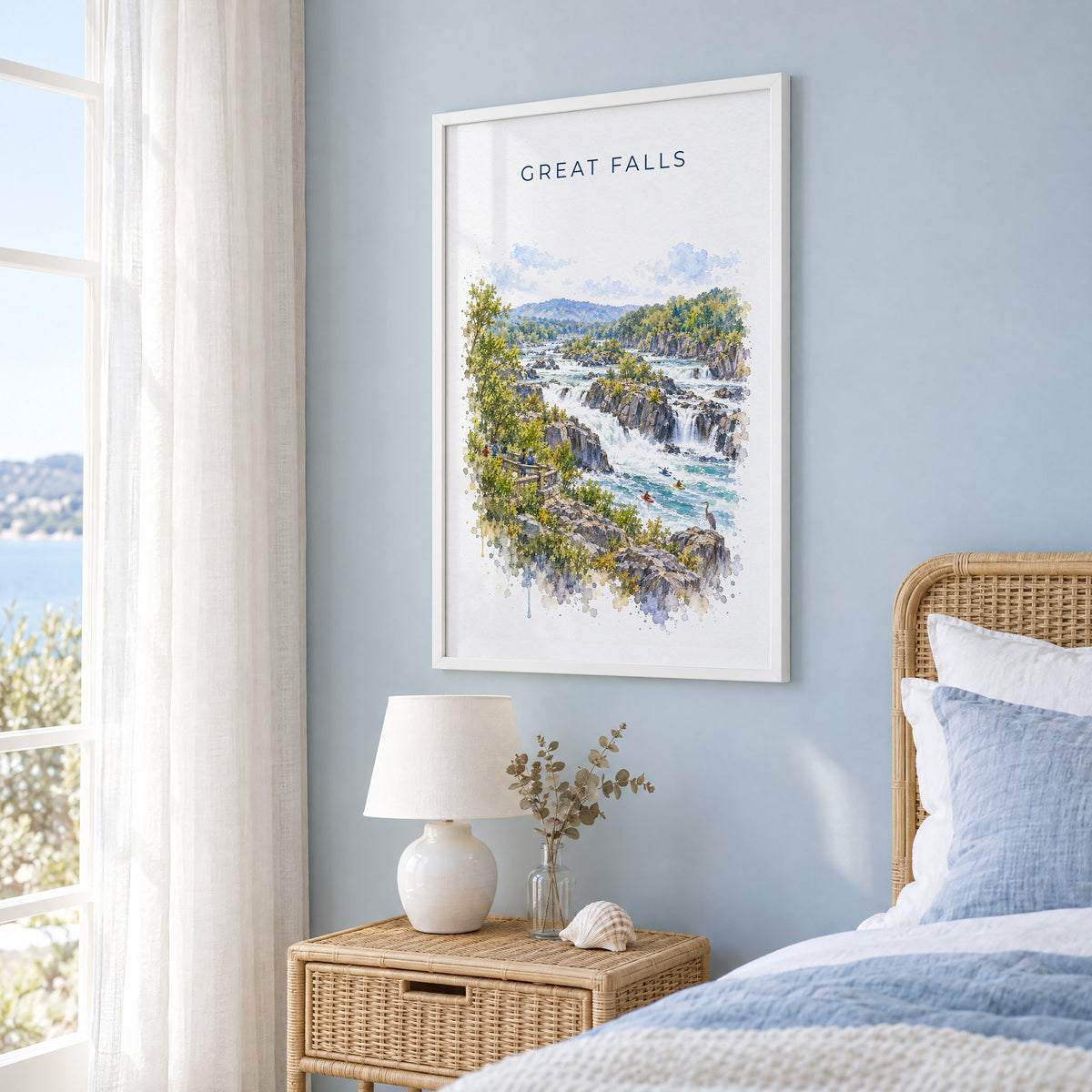 Great Falls Park watercolor print in a white frame on a pale blue wall beside a rattan bed in a coastal bedroom
