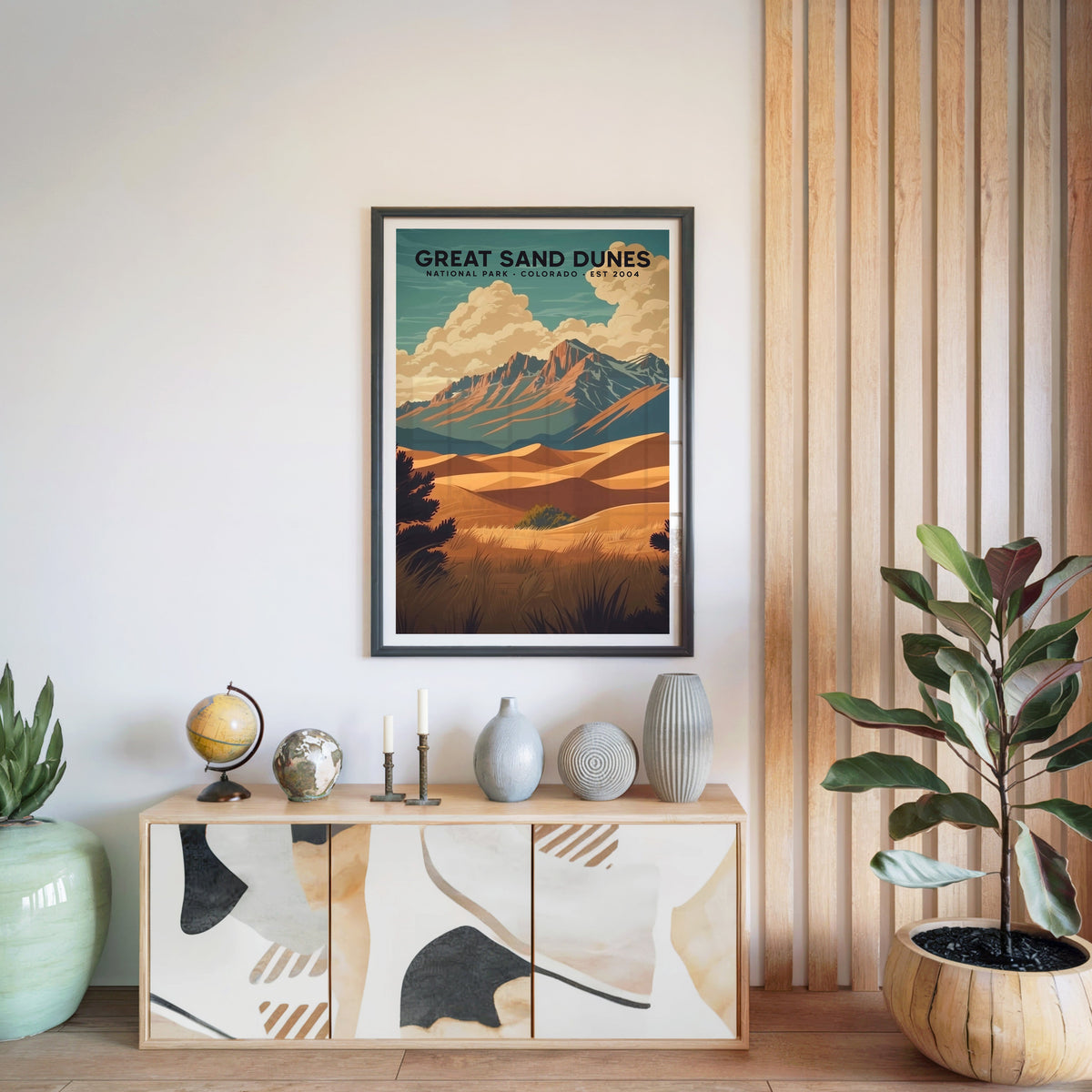 Great Sand Dunes print in a black frame above a light wood sideboard with a globe and vases