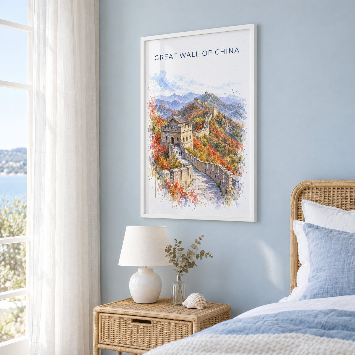 Great Wall of China watercolor print in a white frame on a pale blue wall beside a rattan bed in a coastal bedroom