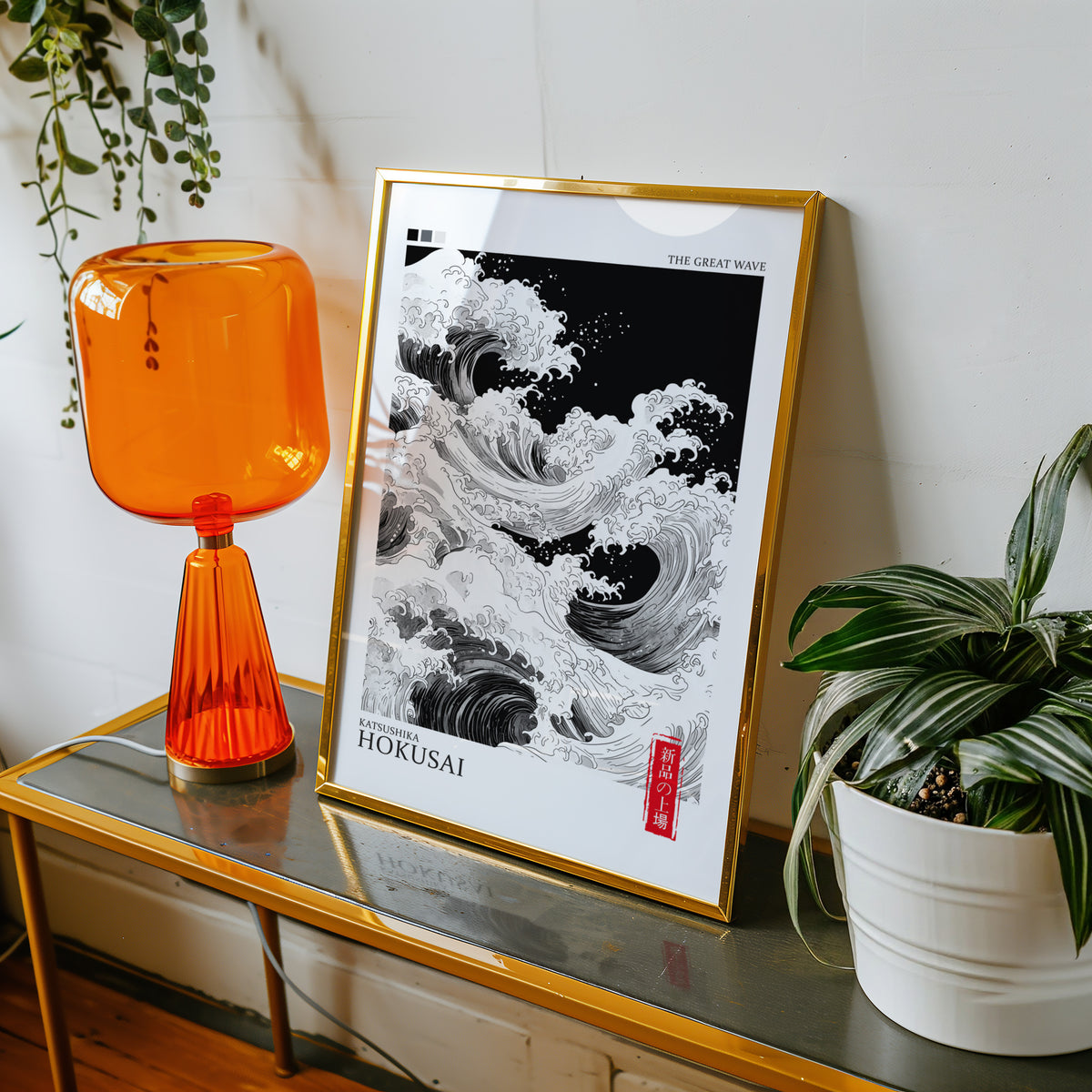 Black and white Great Wave print shown in a gold frame on a console beside an orange glass lamp