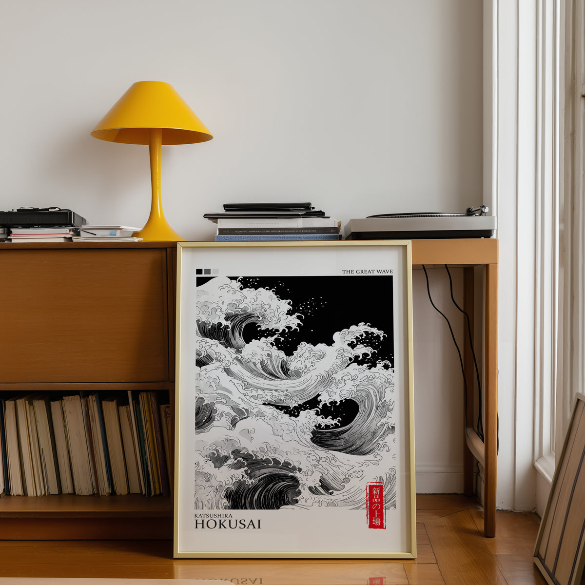 Black and white Great Wave print shown in a gold frame below a teak desk with a yellow lamp