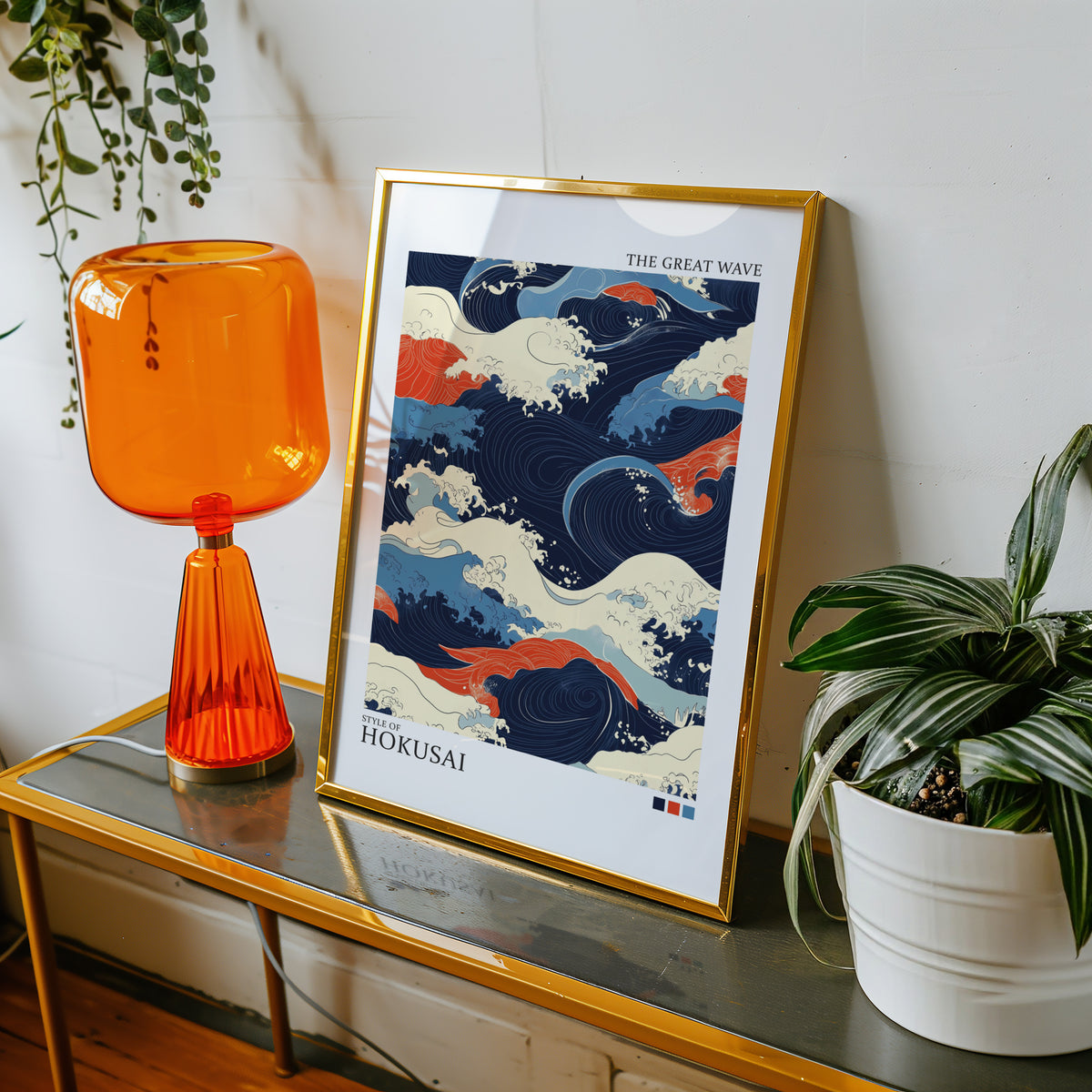 Navy and orange Great Wave print shown in a gold frame on a console beside an orange glass lamp