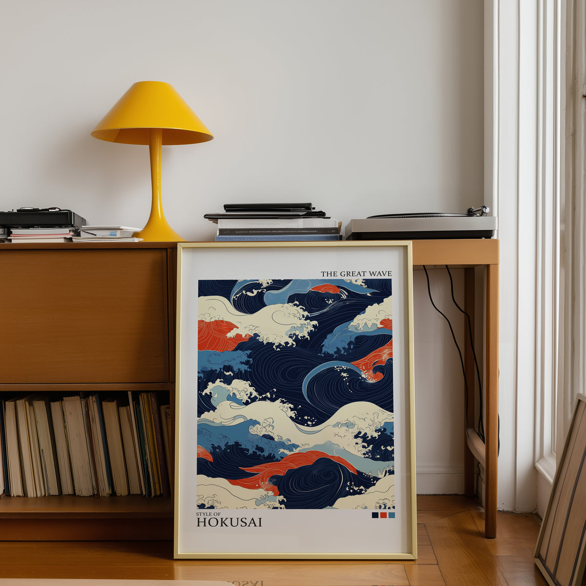 Navy and orange Great Wave print shown in a gold frame below a teak desk with a yellow lamp