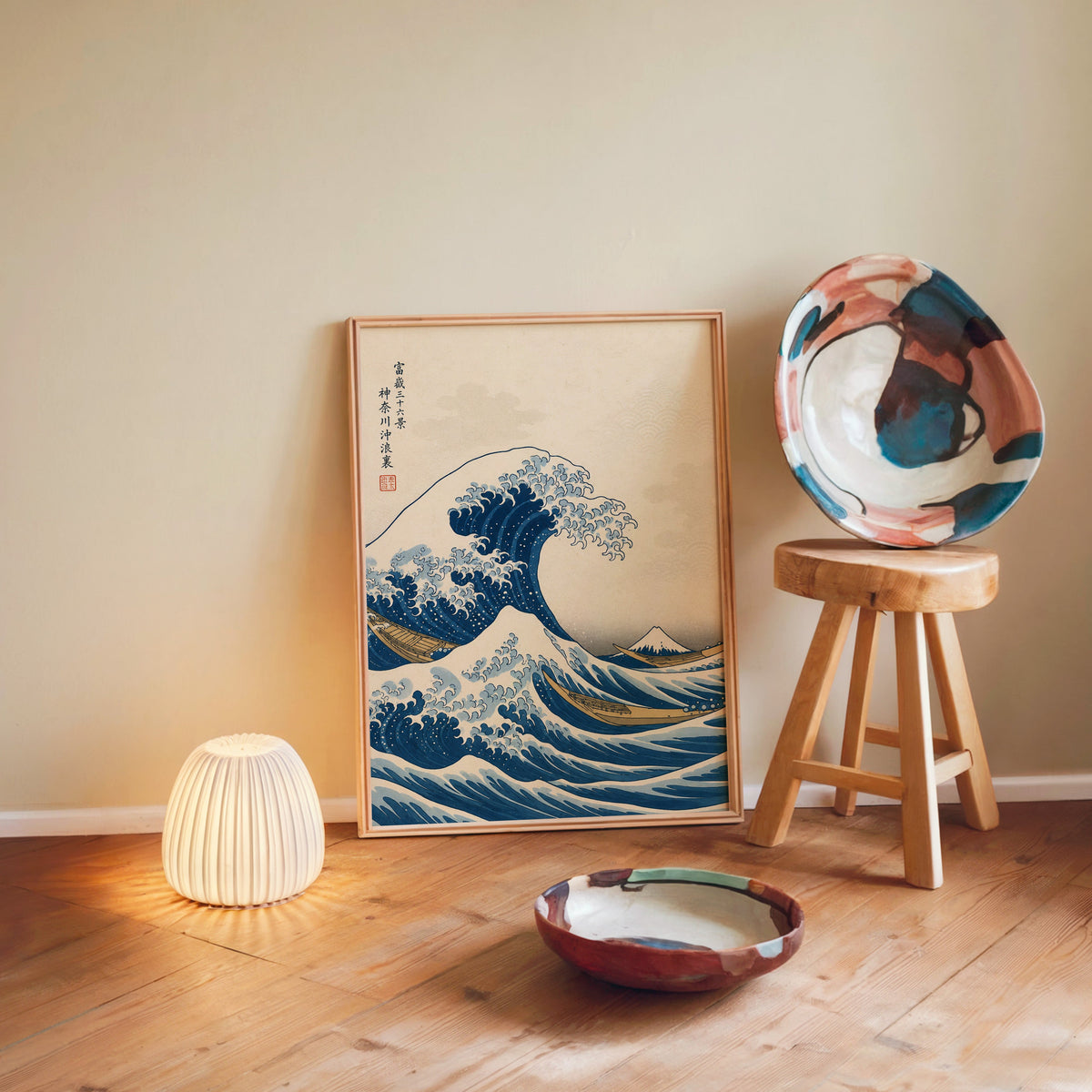 Great Wave off Kanagawa print in a light wood frame leaning on a wooden floor by a glowing lamp and stool