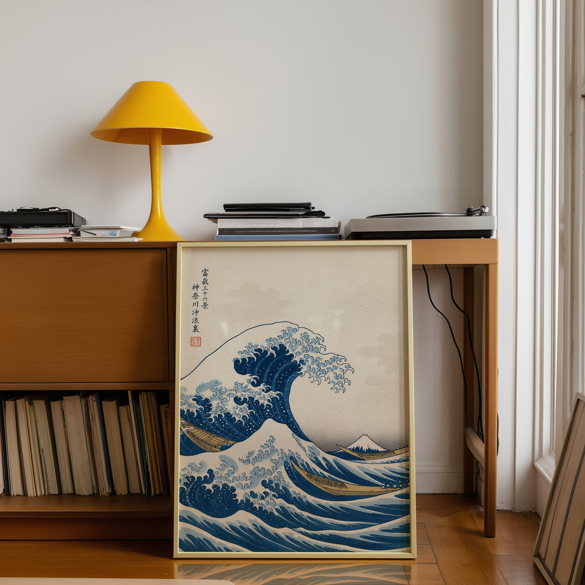 Great Wave off Kanagawa print shown in a gold frame leaning under a teak desk with a yellow lamp
