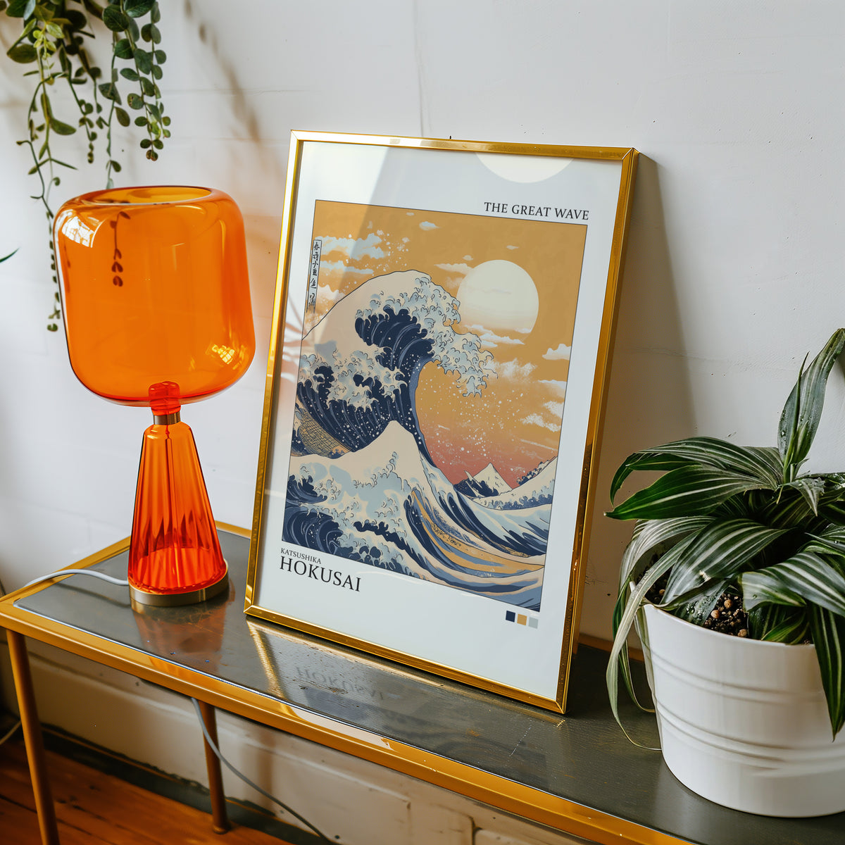 Great Wave under orange sky print shown in a gold frame on a console beside an orange glass lamp