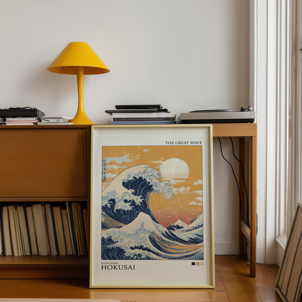Great Wave under orange sky print shown in a gold frame below a teak desk with a yellow lamp