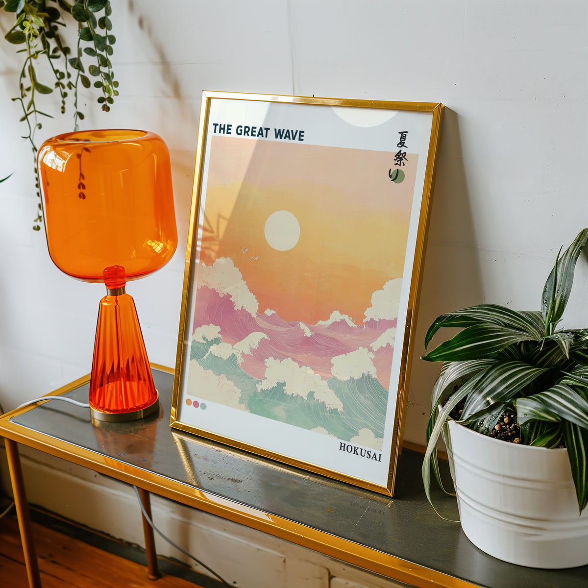 Pastel Great Wave sunset print shown in a gold frame on a console beside an orange glass lamp