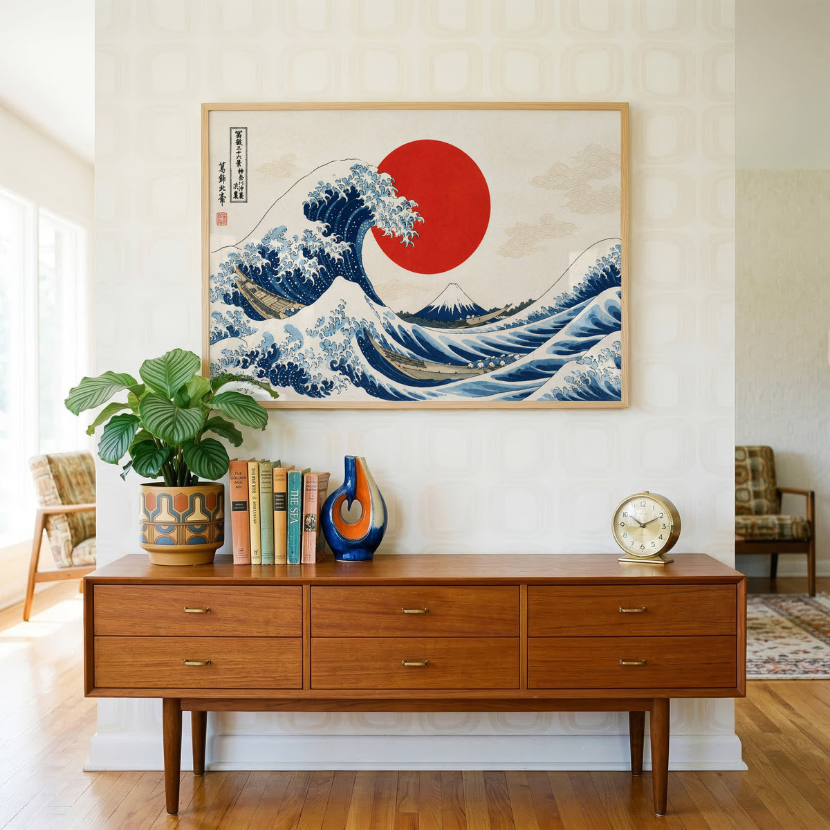 Great Wave with a red sun print in a light oak frame above a teak credenza with books and a brass clock