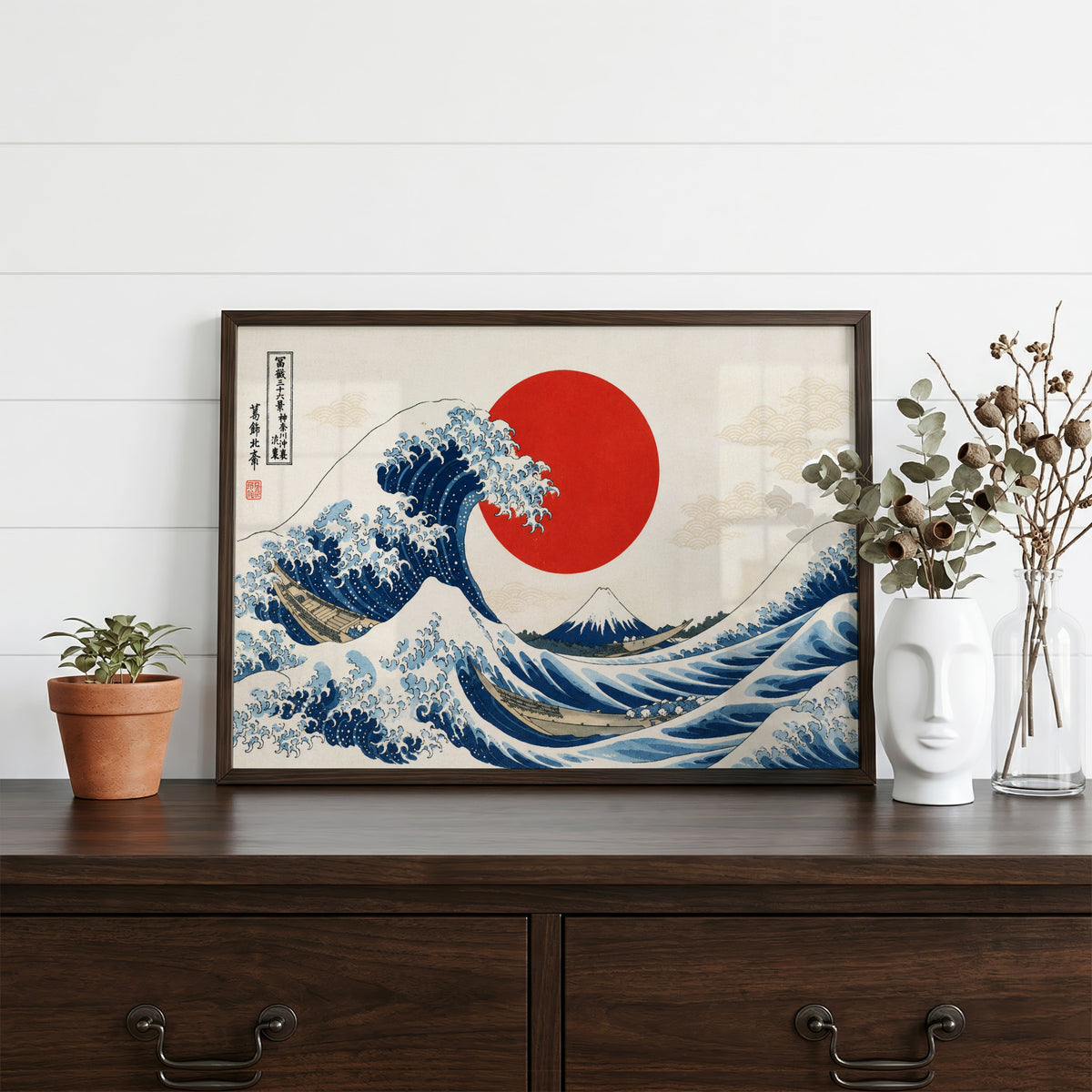 Great Wave with a red sun print in a dark walnut frame on a dark wood dresser beside a white face vase