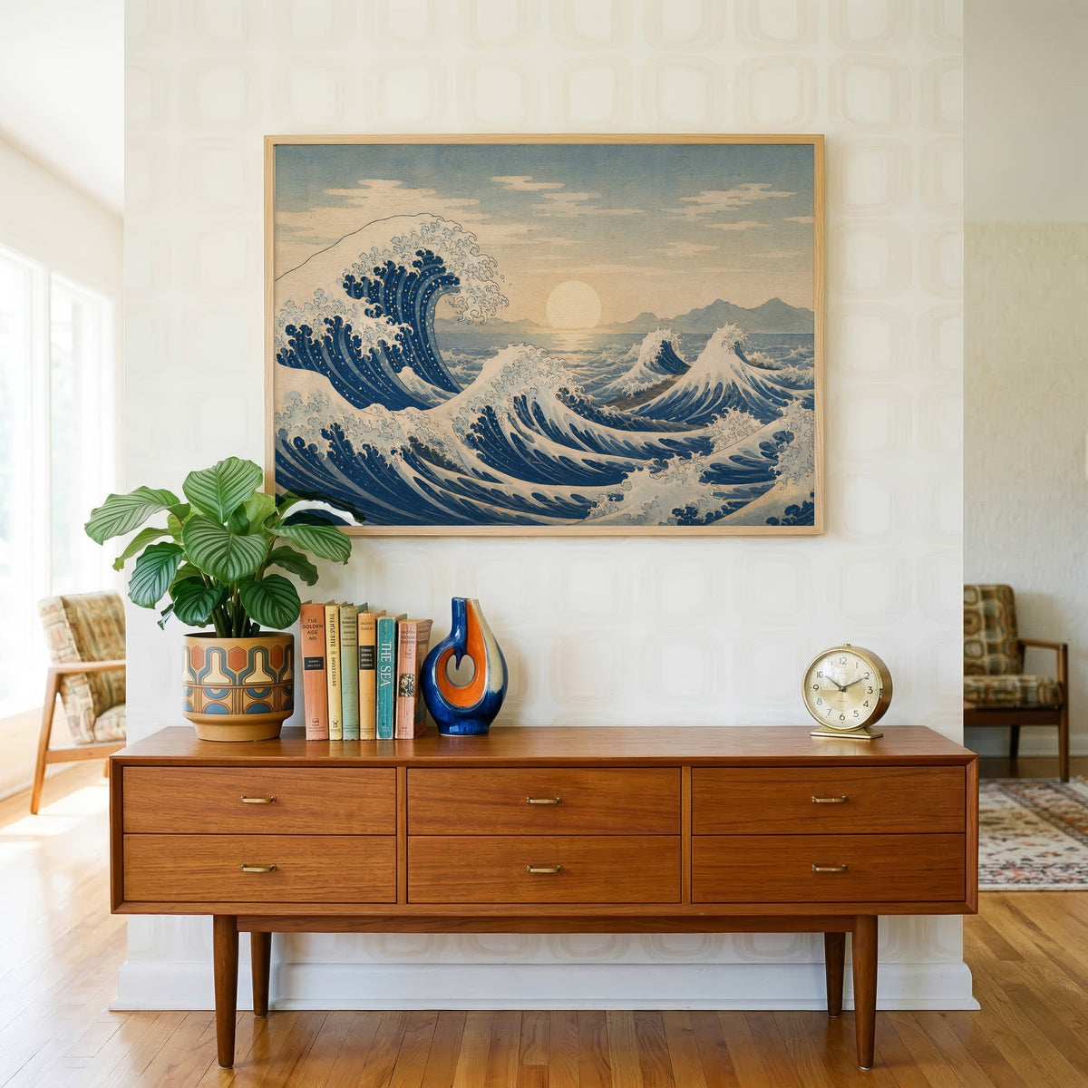 Great wave at sunrise over the sea print in a light oak frame above a teak credenza with books and a brass clock