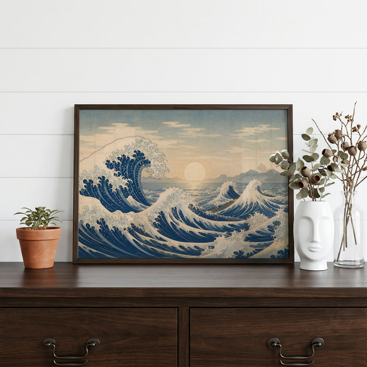 Great wave at sunrise over the sea print in a dark walnut frame on a dark wood dresser beside a white face vase