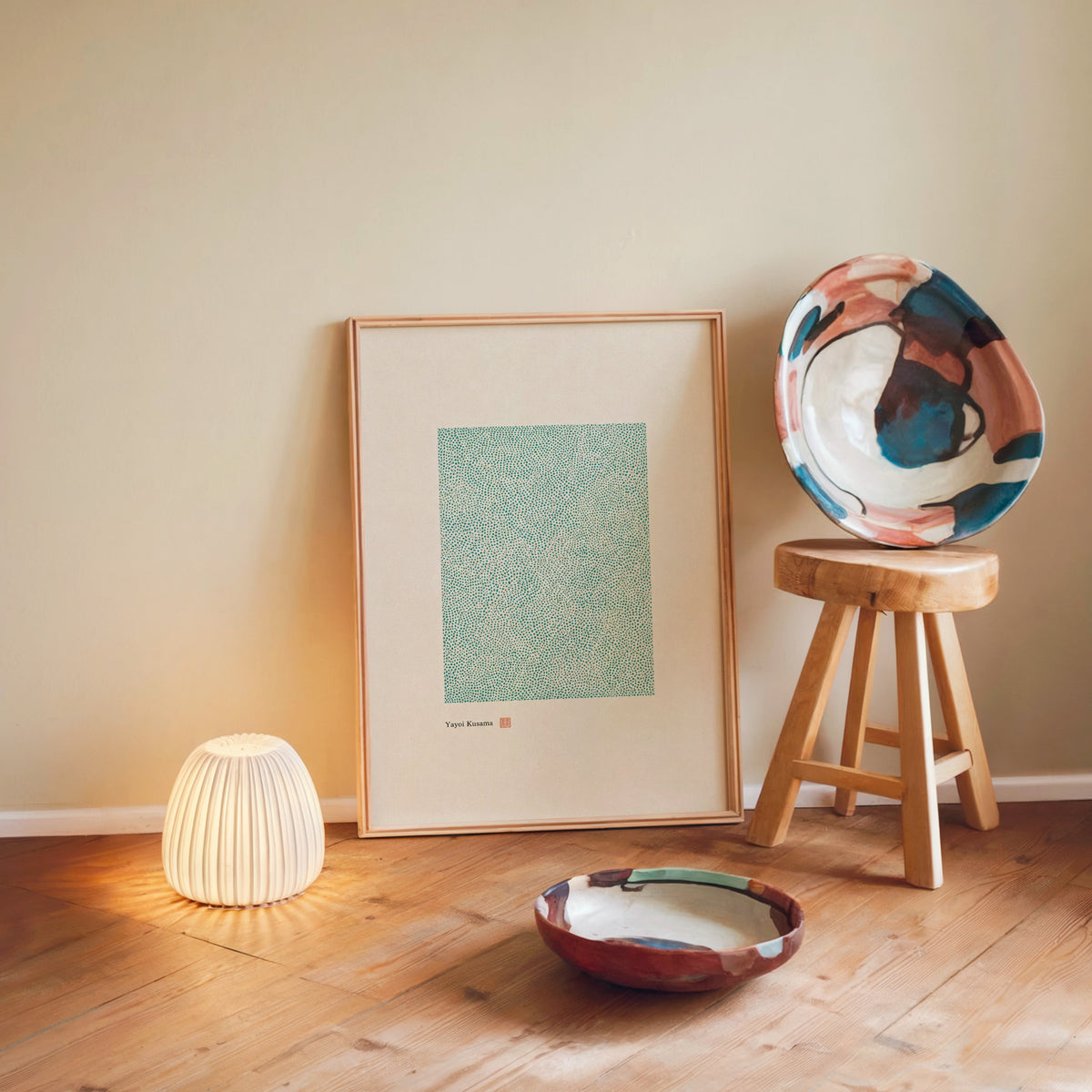 green dot field abstract print in a light wood frame leaning on a wooden floor by a glowing lamp and stool
