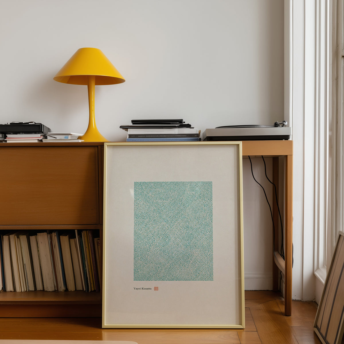 green dot field abstract print shown in a gold frame leaning under a teak desk with a yellow lamp