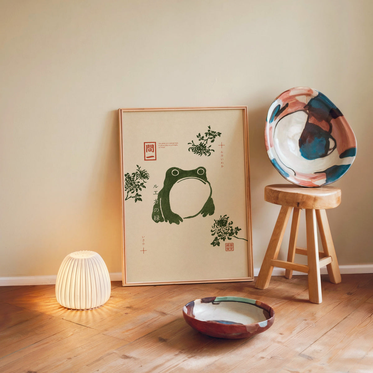 green frog with chrysanthemums print in a light wood frame leaning on a wooden floor by a glowing lamp and stool