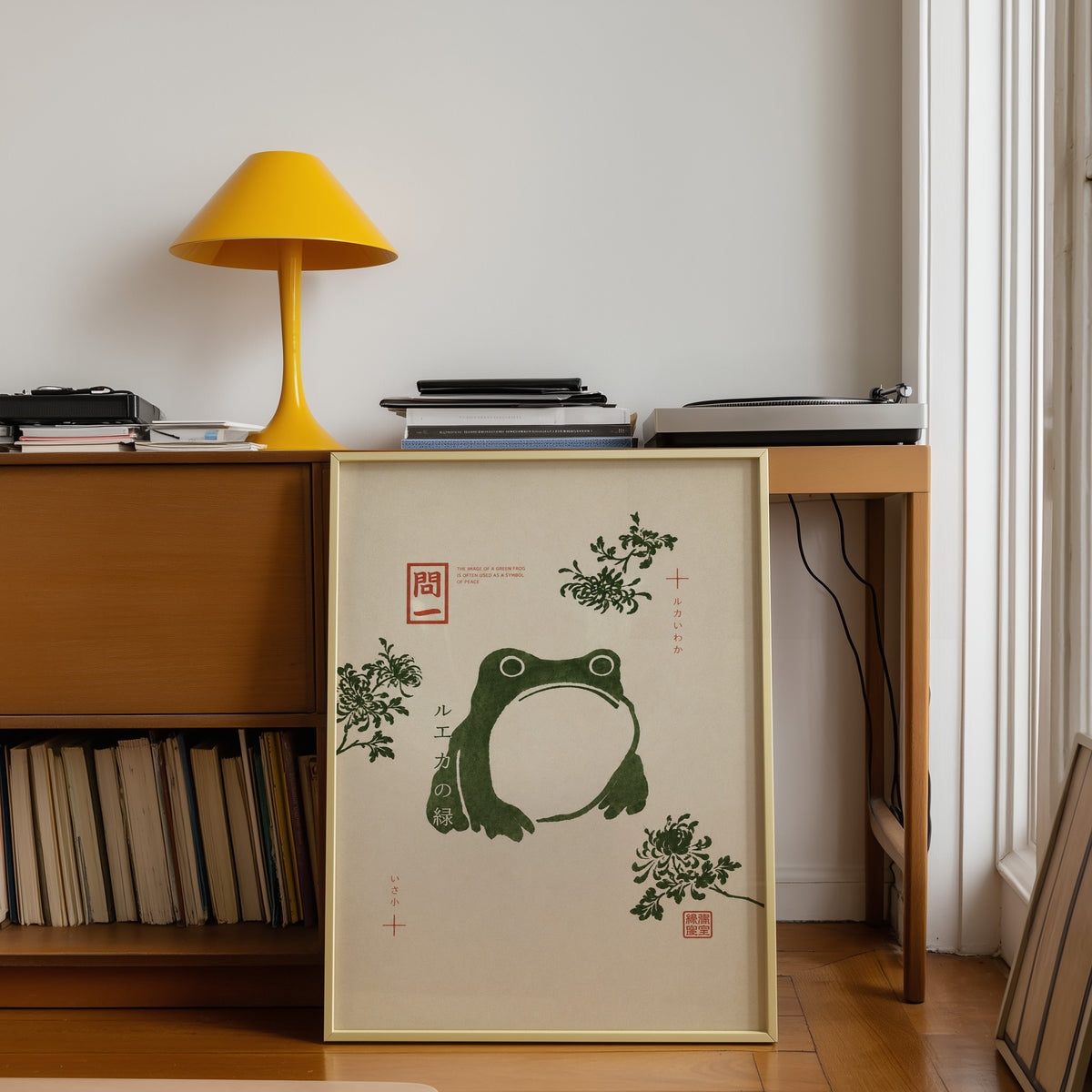 green frog with chrysanthemums print shown in a gold frame leaning under a teak desk with a yellow lamp