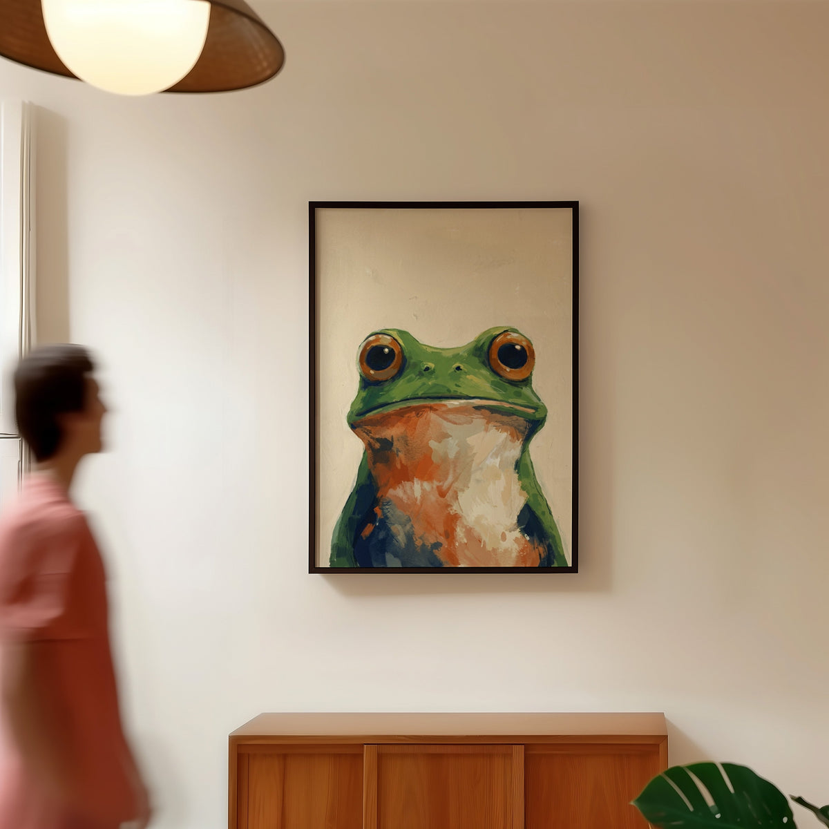 Cream and green frog print in a black frame in a hallway under a rattan pendant