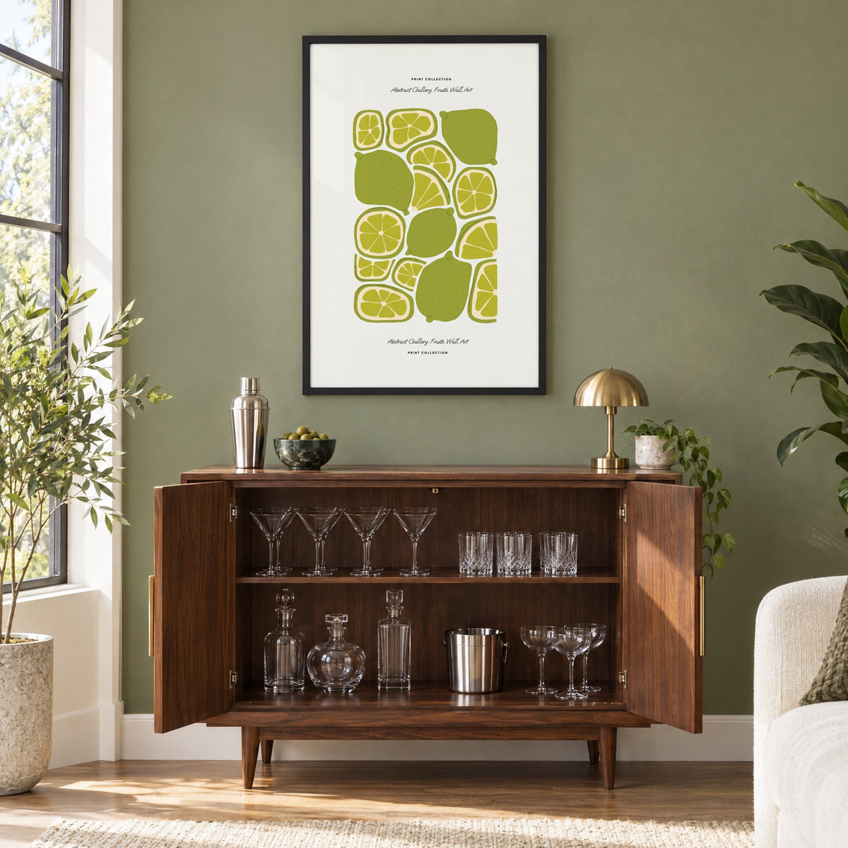 green lime slices pattern fruit print in a black frame on an olive green wall above a walnut bar cabinet with glassware