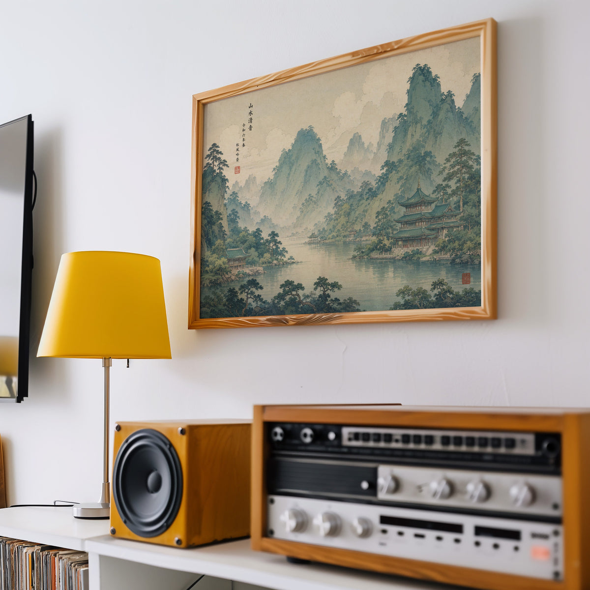 Green mountain lake with temples print in a pine frame above a vintage stereo and a yellow table lamp