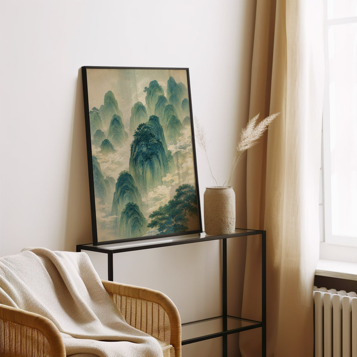 green mountains and clouds landscape print in a black frame leaning on a glass console beside pampas grass
