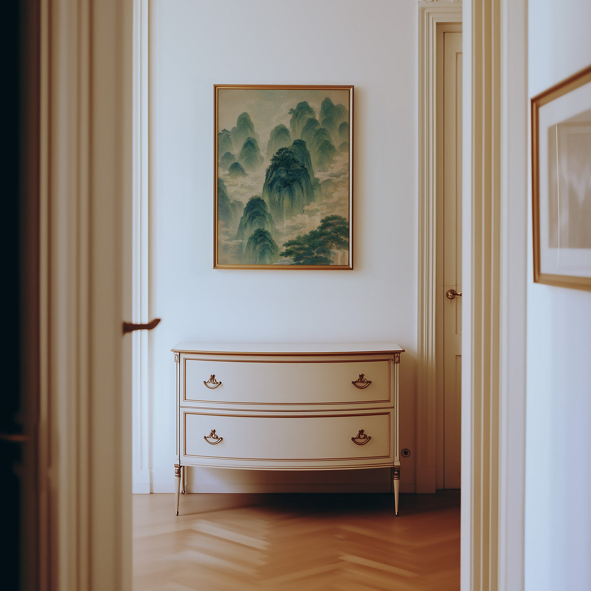green mountains and clouds landscape print shown in a gold frame in a hallway above a cream dresser