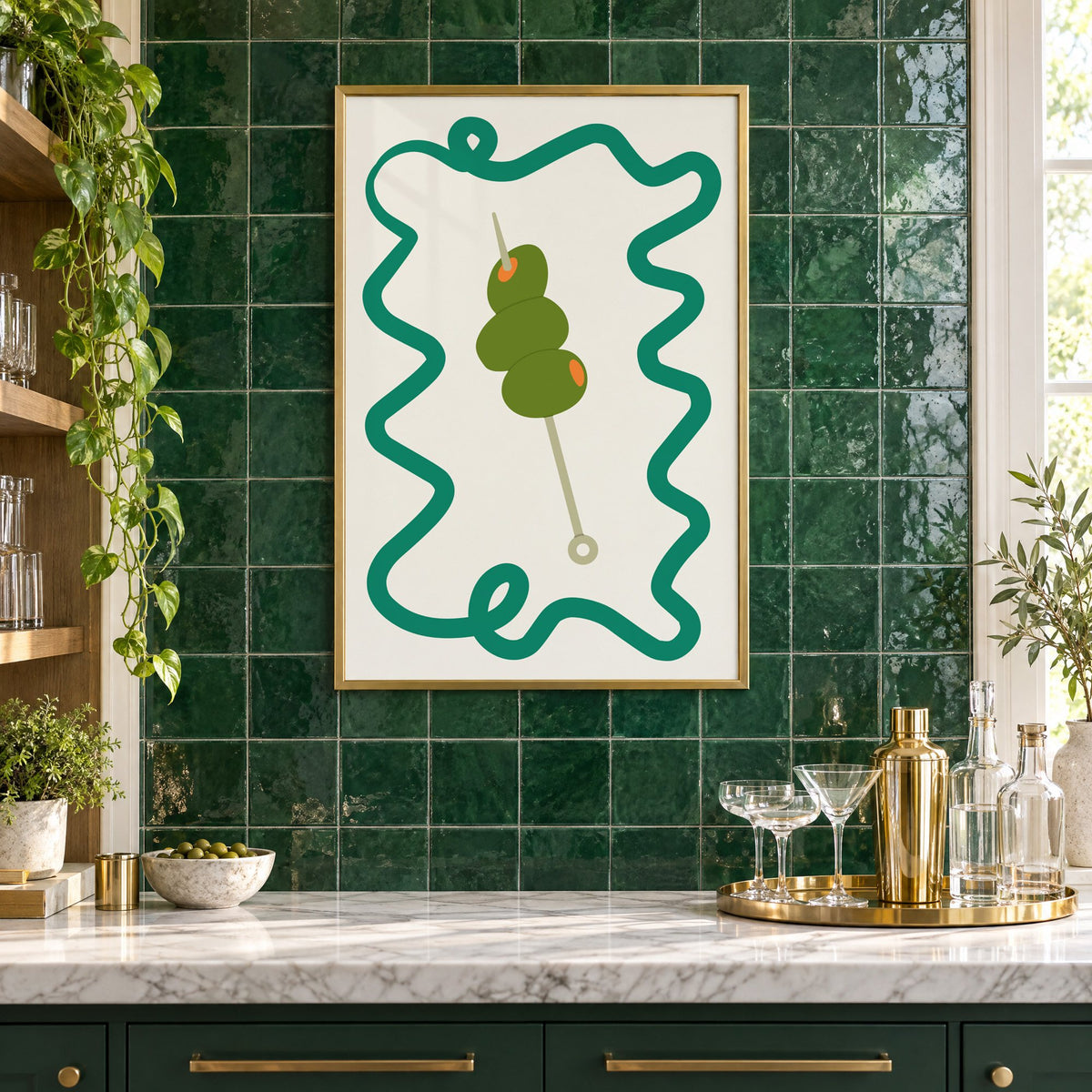 Green olives cocktail pick print in a brass frame on emerald green tiles above a home bar with coupe glasses
