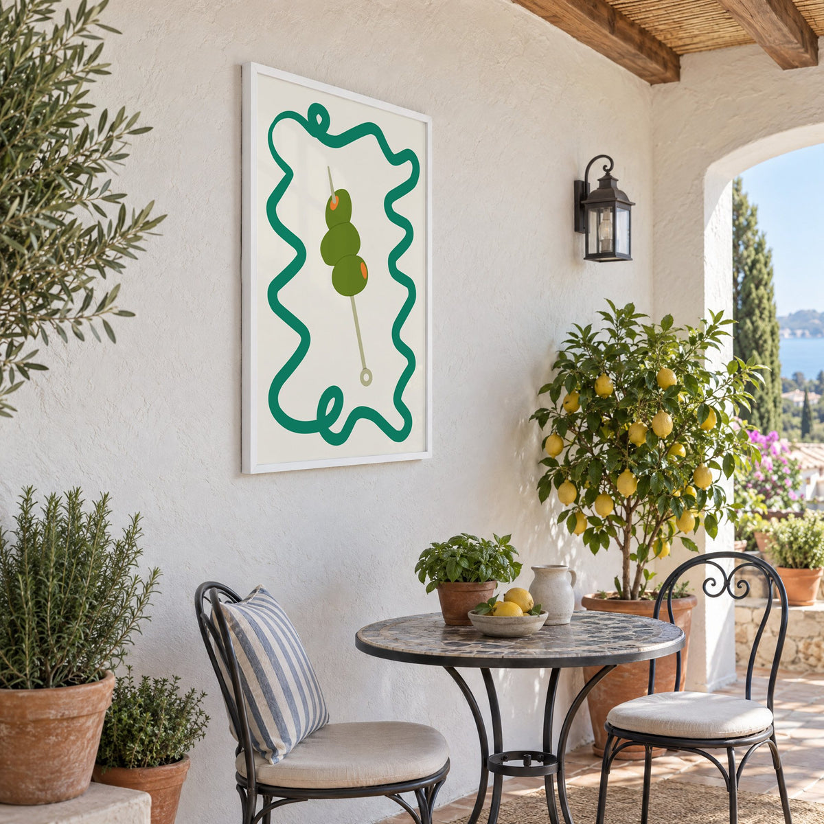Green olives cocktail pick print in a white frame on a sunny patio wall beside a potted lemon tree