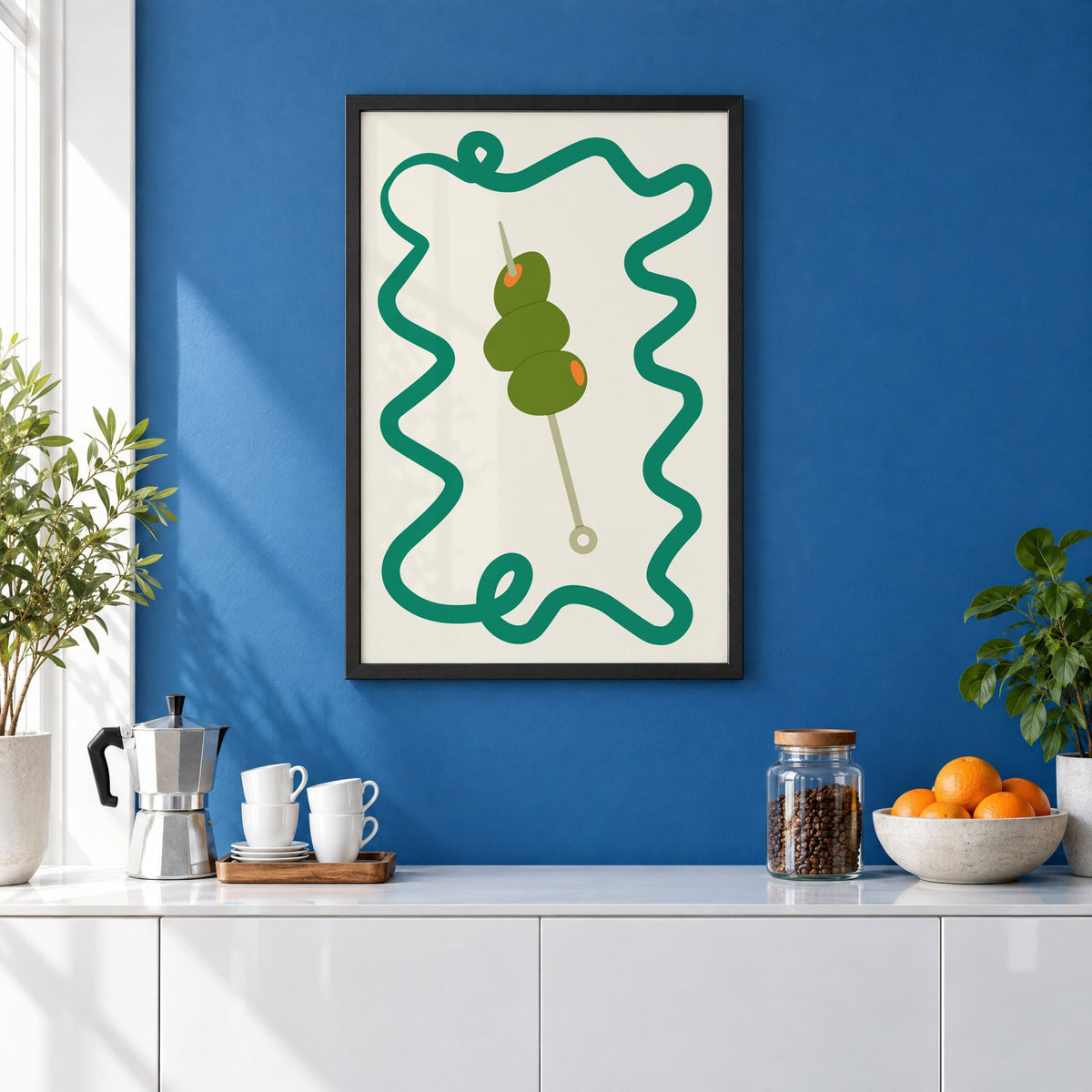 Green olives cocktail pick print in a black frame on a cobalt blue wall above a coffee station