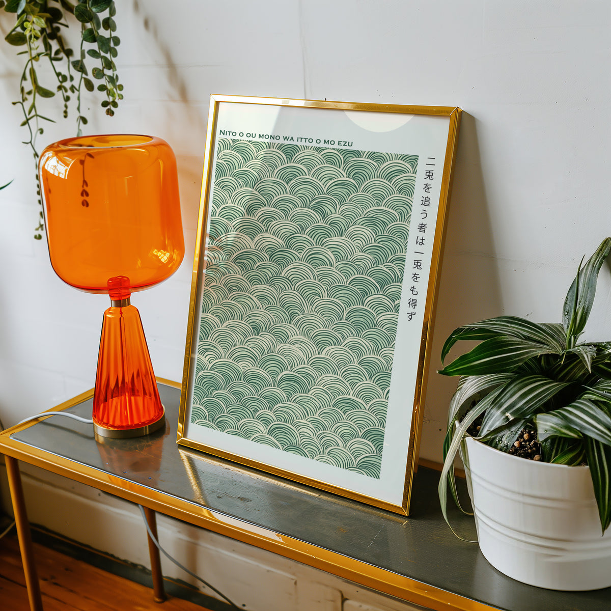 Green seigaiha wave proverb print shown in a gold frame on a console beside an orange glass lamp