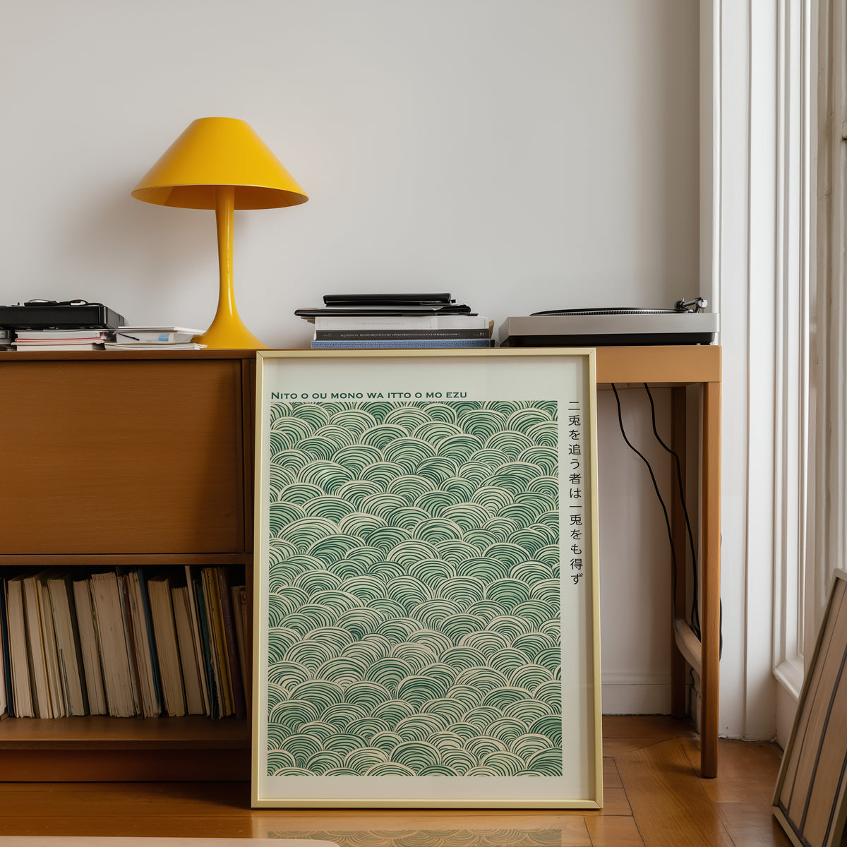 Green seigaiha wave proverb print shown in a gold frame below a teak desk with a yellow lamp