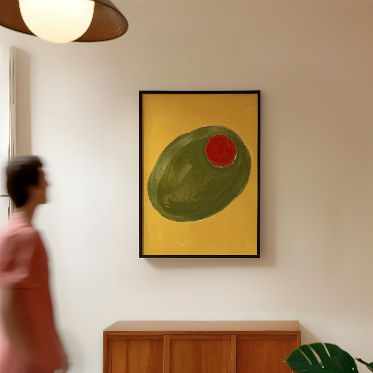 Mustard and olive green print in a black frame in a hallway under a rattan pendant