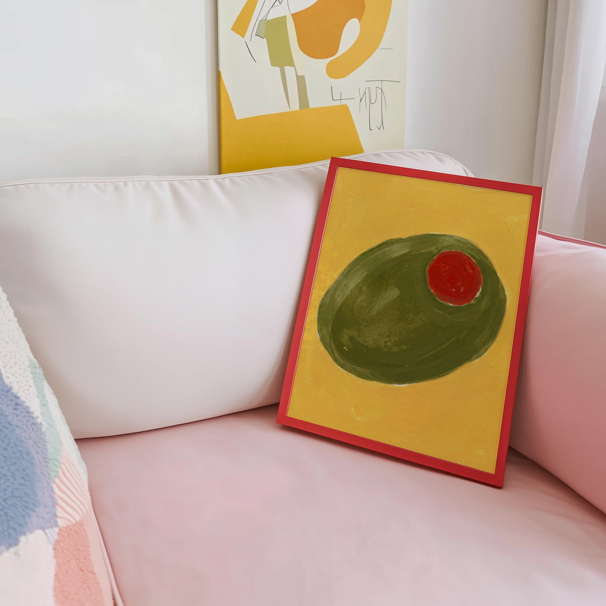 Giant olive still life print shown in a red frame leaning on a blush pink sofa