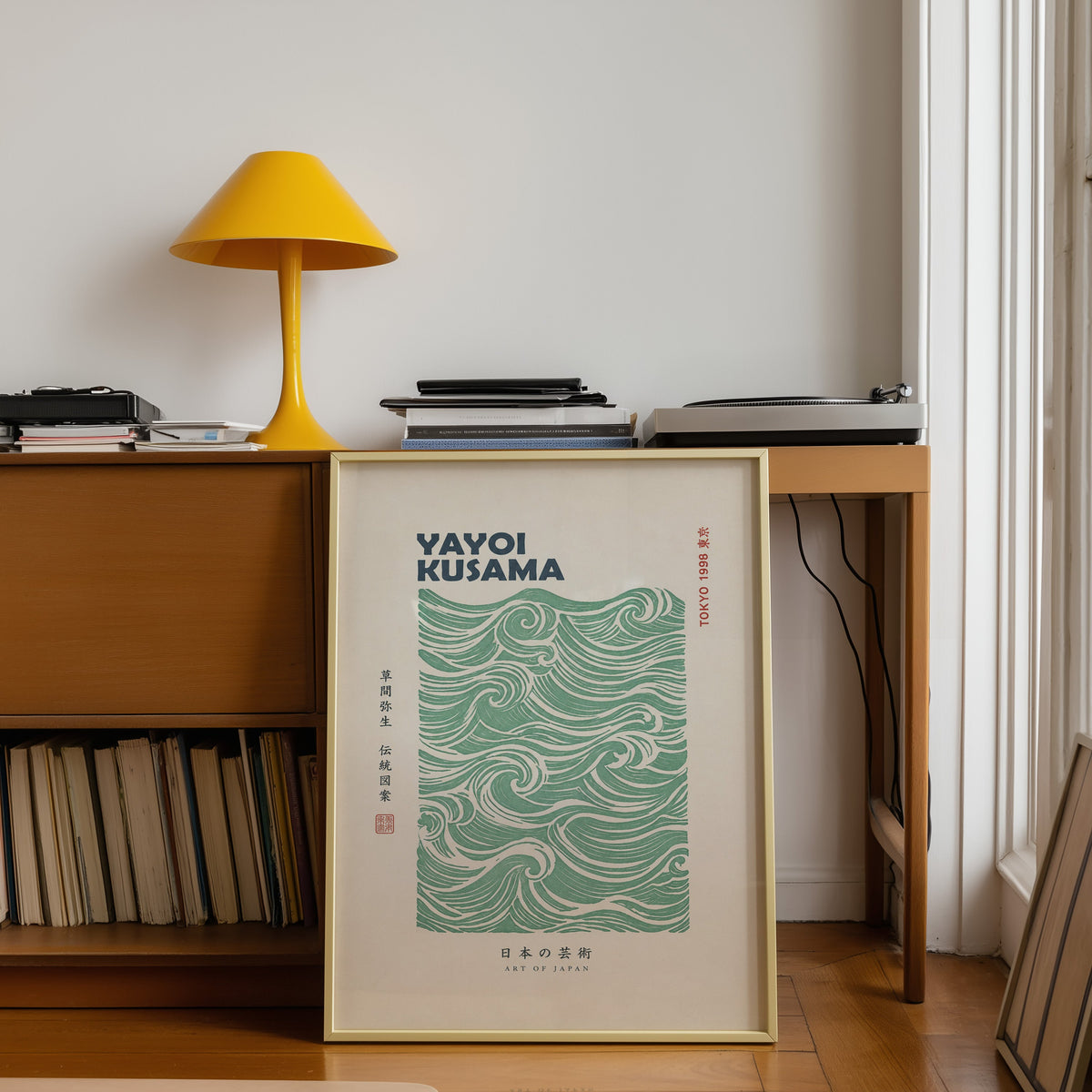 green wave pattern with bold type print shown in a gold frame leaning under a teak desk with a yellow lamp