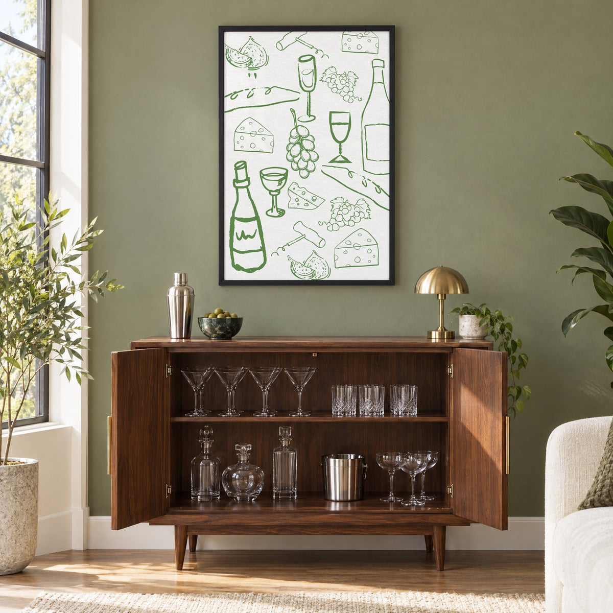 Green wine and cheese doodle pattern print in a black frame on an olive green wall above a walnut bar cabinet with glassware