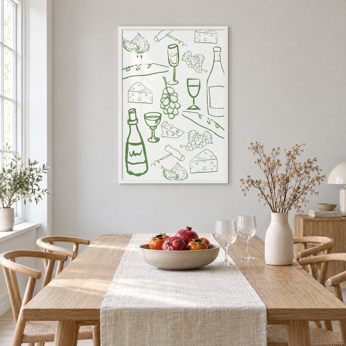 Green wine and cheese doodle pattern print in a white frame above a light oak dining table with a linen runner and fruit bowl