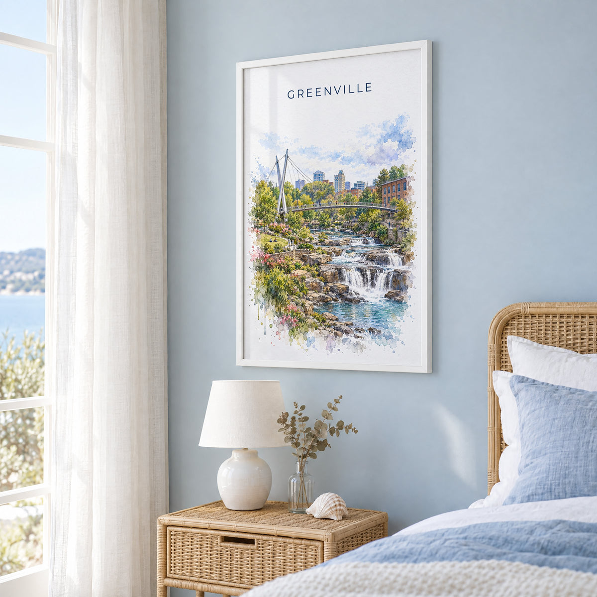 Greenville, South Carolina watercolor print in a white frame on a pale blue wall beside a rattan bed in a coastal bedroom
