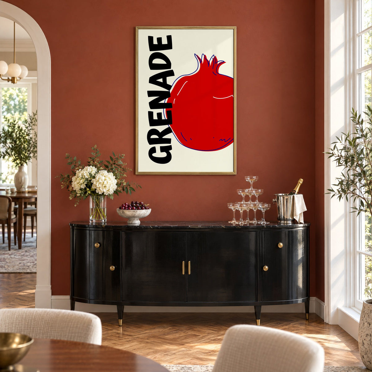 GRENADE red pomegranate print in a brass frame on a terracotta wall above a black buffet with a champagne tower