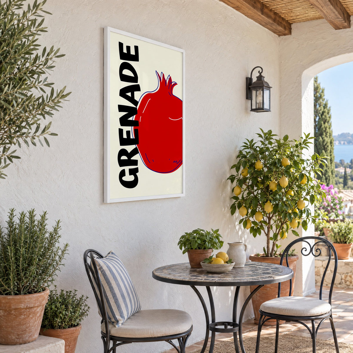 GRENADE red pomegranate print in a white frame on a sunny patio wall beside a potted lemon tree