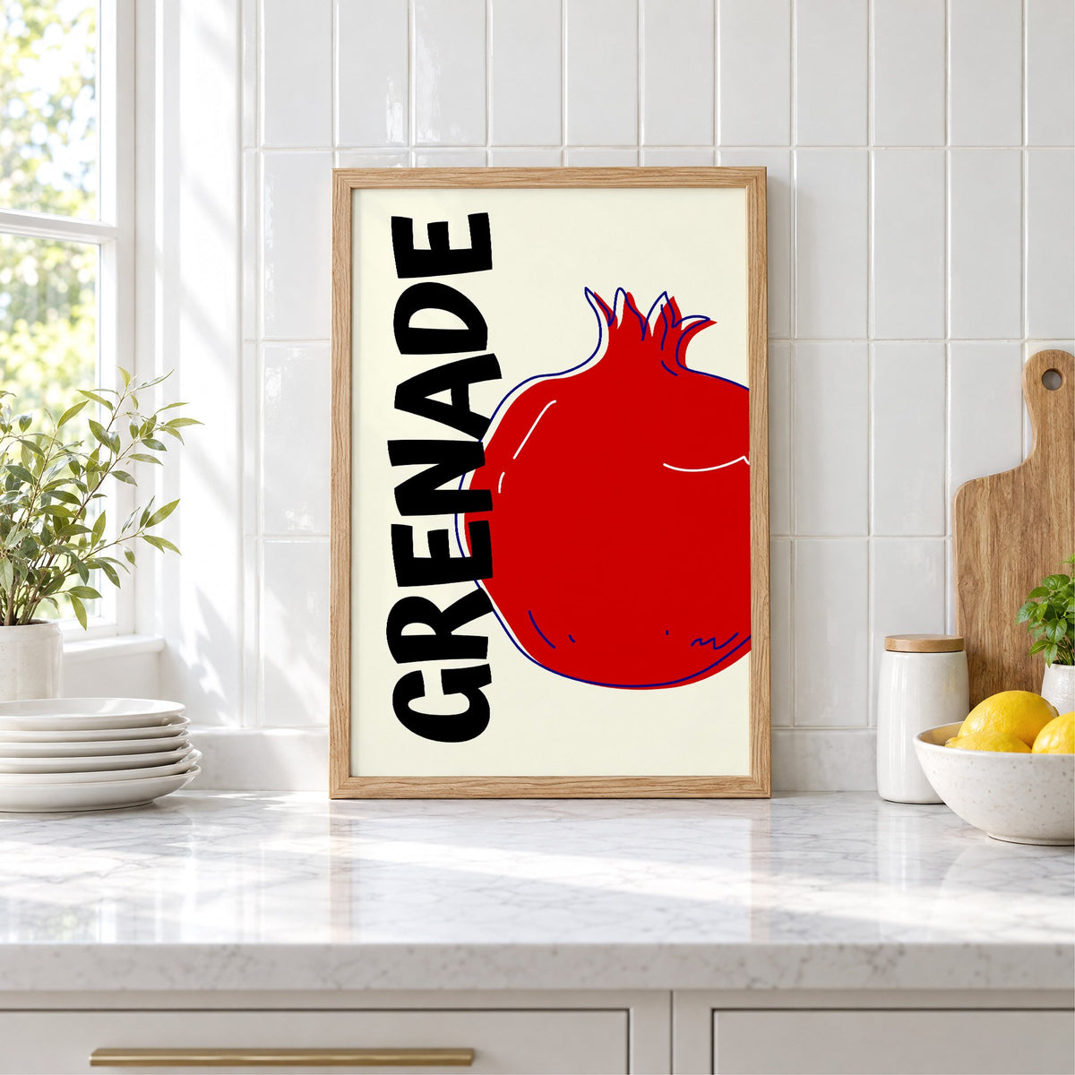 GRENADE red pomegranate print in an oak frame leaning on a marble counter by white tiles and lemons