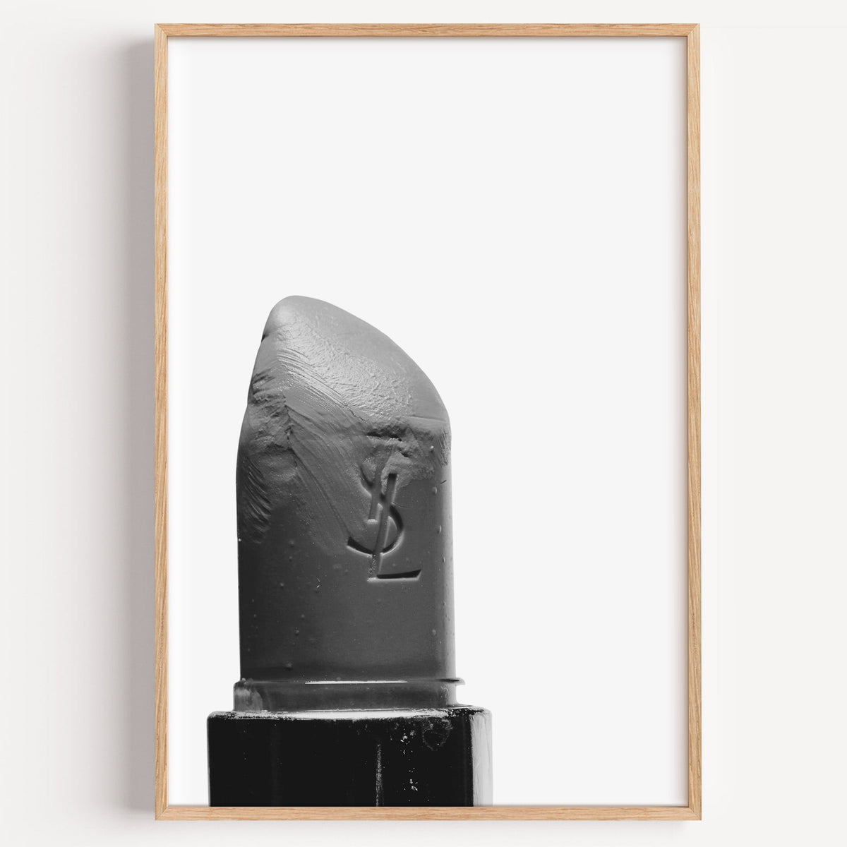 Angled lipstick bullet on plain white print in a light oak frame on a plain white wall