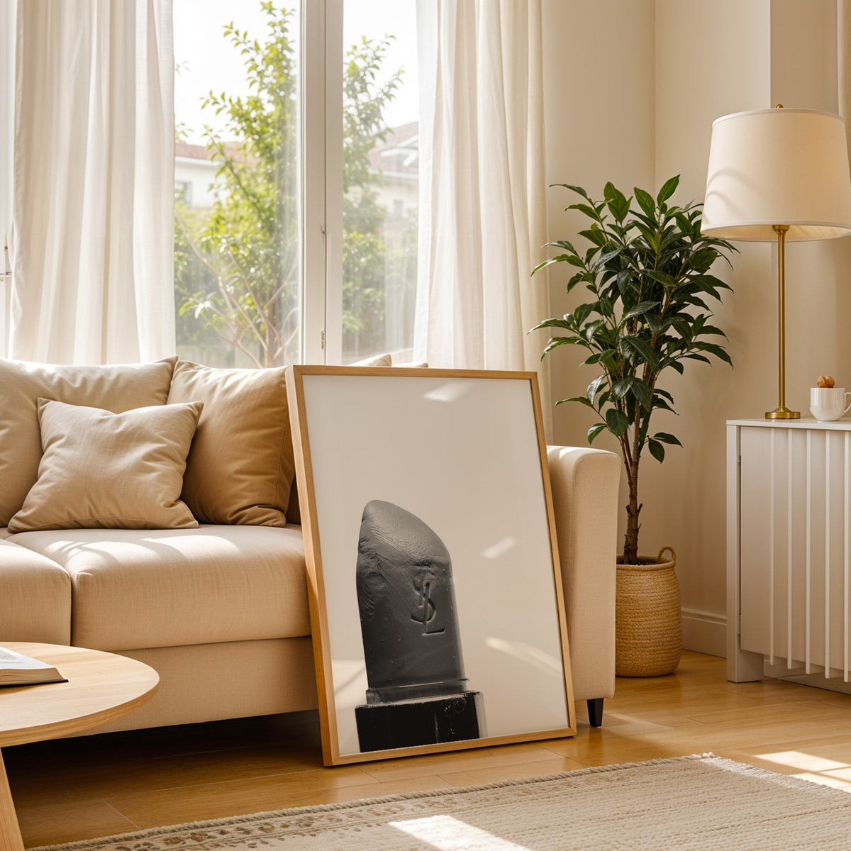Angled lipstick bullet on plain white print in a light oak frame leaning on a cream sofa beside a floor lamp