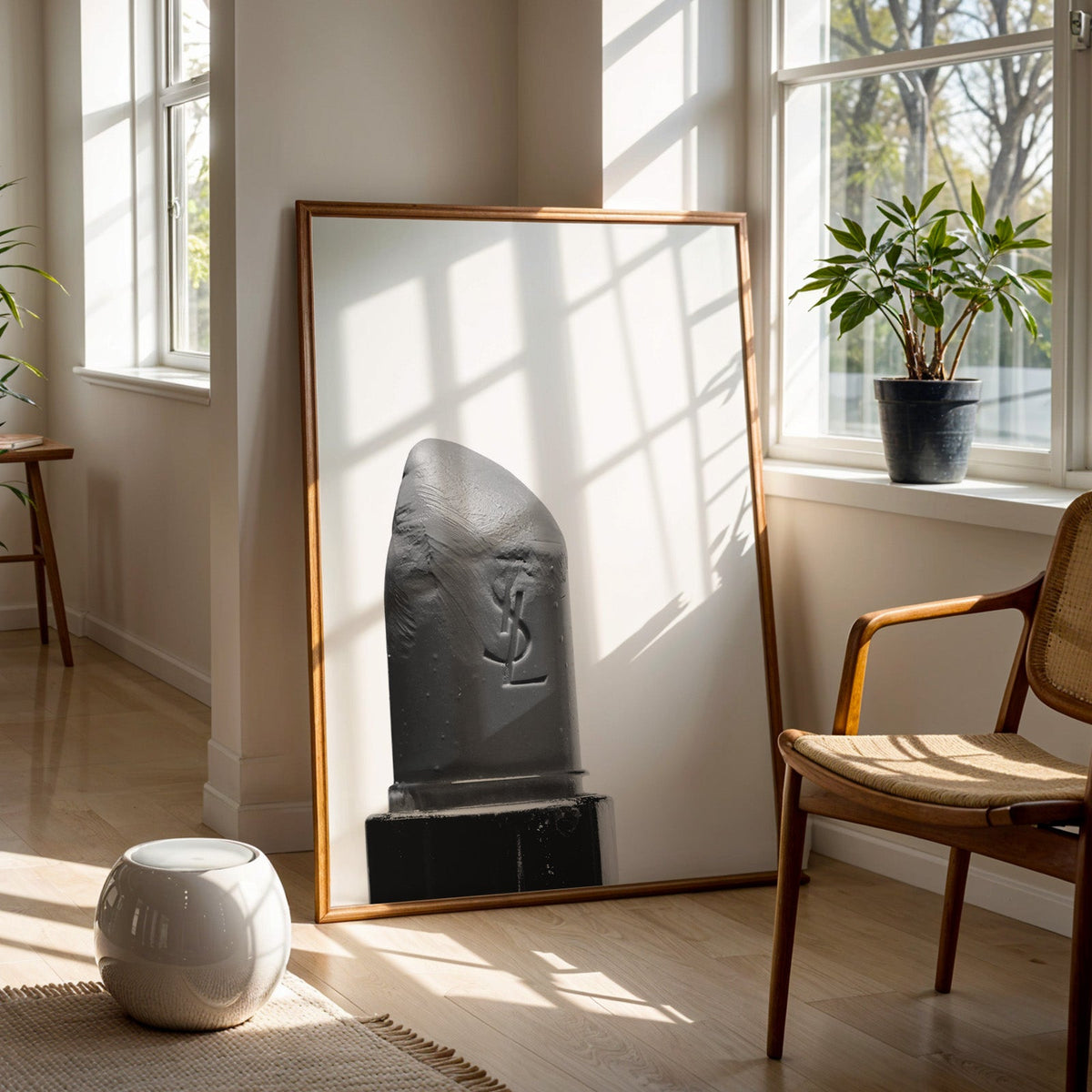 Angled lipstick bullet on plain white print in a walnut frame on a wood floor beside a cane chair and sunny window