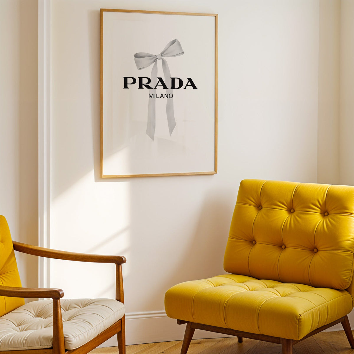 Soft grey silk bow with long ribbon tails print shown in a gold frame above a mustard yellow tufted armchair