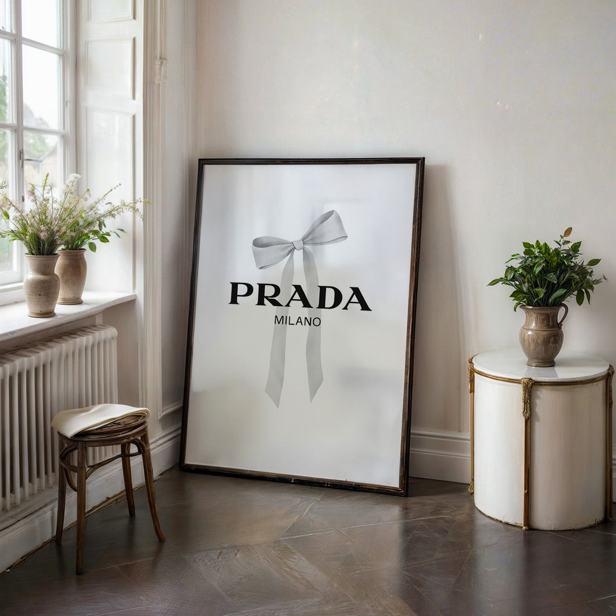 Soft grey silk bow with long ribbon tails print in a black frame on a dark stone floor beside a white side table
