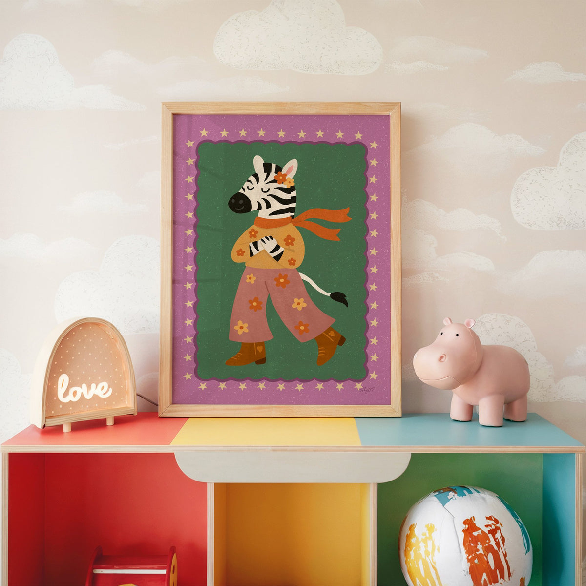 Groovy zebra in flower pants nursery print in an oak frame on a rainbow toy shelf against cloud wallpaper