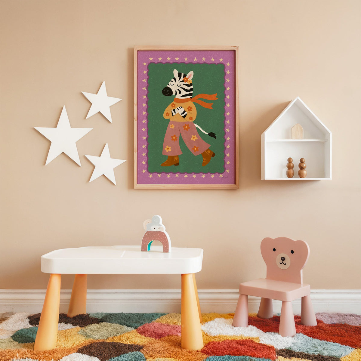 Groovy zebra in flower pants nursery print in an oak frame on a peach wall above a kids table with wall stars