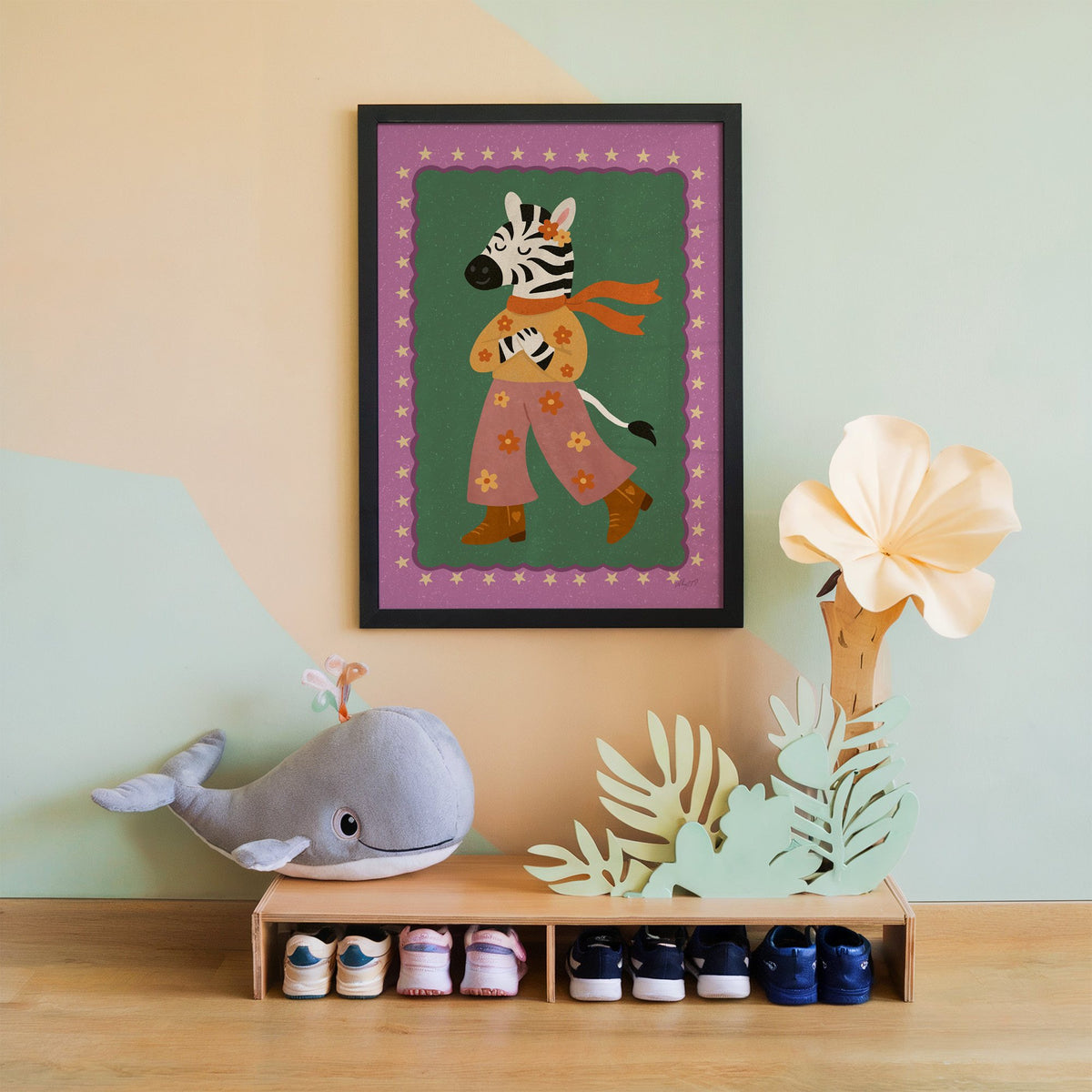 Groovy zebra in flower pants nursery print in a black frame on a mint and peach wall above a whale plush