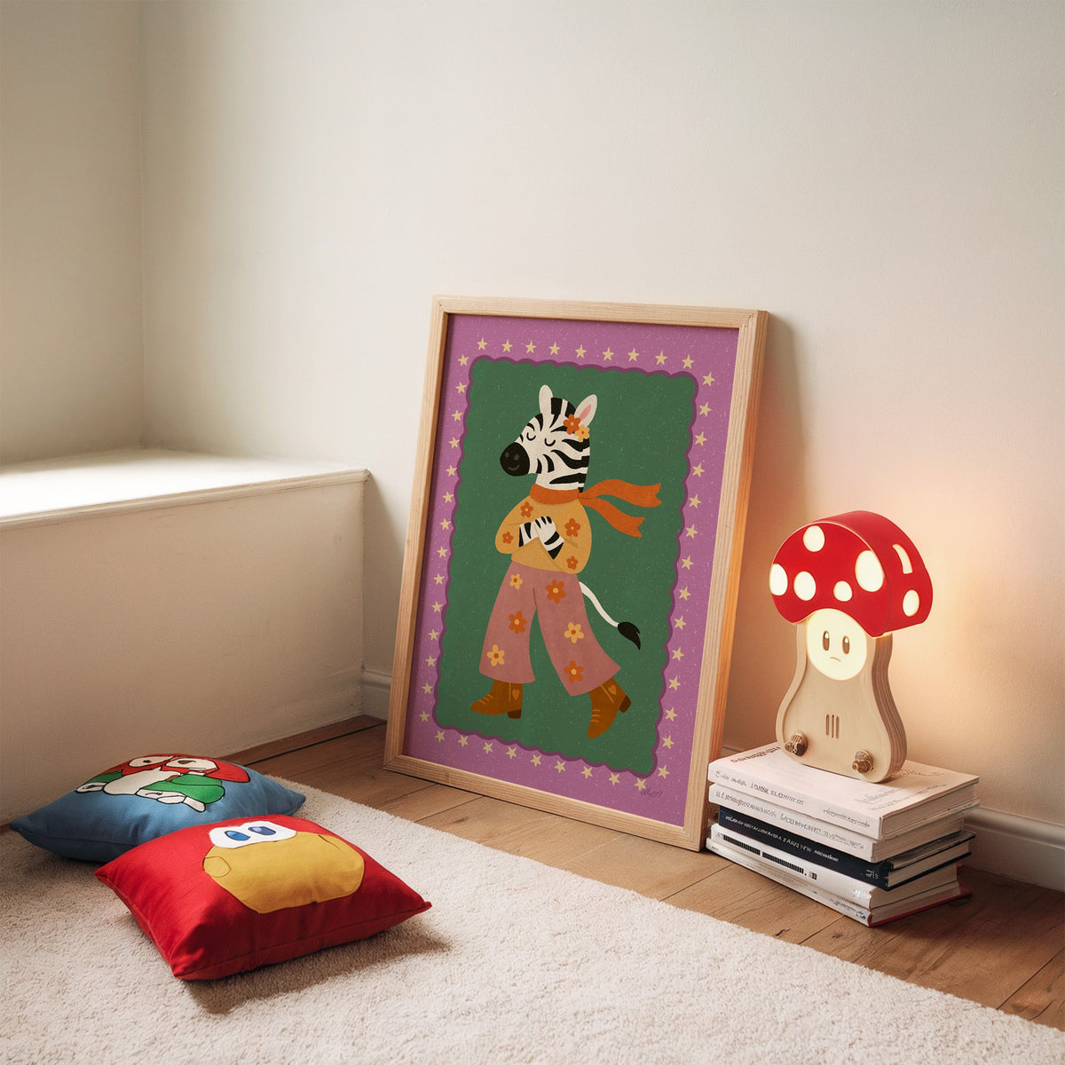 Groovy zebra in flower pants nursery print in an oak frame leaning on a rug beside a mushroom lamp and floor cushions